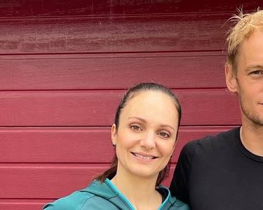 Die ehemalige Eiskunstläuferin Sarah van Berkel steht mit ihrem Partner vor eine roten Wand.