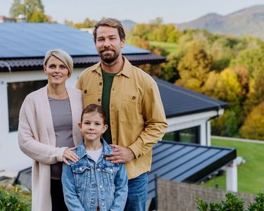 Ehepaar mit Kind steht vor Haus mit Solaranlage